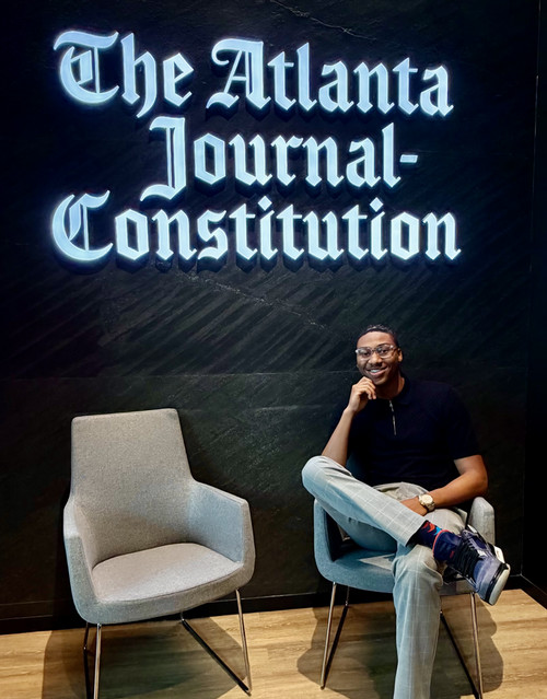 Antonio Mattox Jr. sitting, posing in front of an Atlanta Journal-Constitute sign.